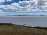 Lake 80% dry; some water at further side; lake floor grey silt covered by crust of salt; appears grey under cloud shade and white in sunlight