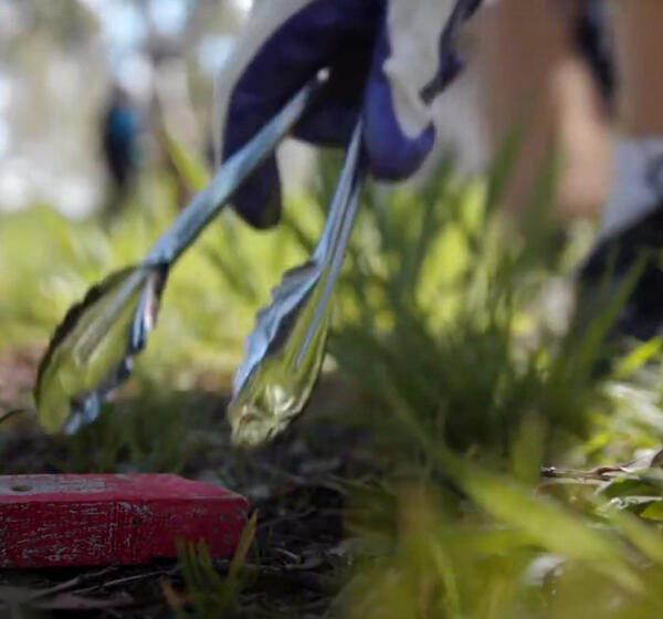 Person wearing gloves uses a pair of tongs to pick up rubbish from the ground